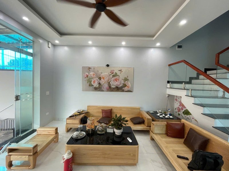 Phòng khách tầng 1 với bộ sofa gỗ và tranh treo tường tại nhà 3 tầng Đoài Phương, Sơn Tây — công trình Nhà Mộc xây trọn gói