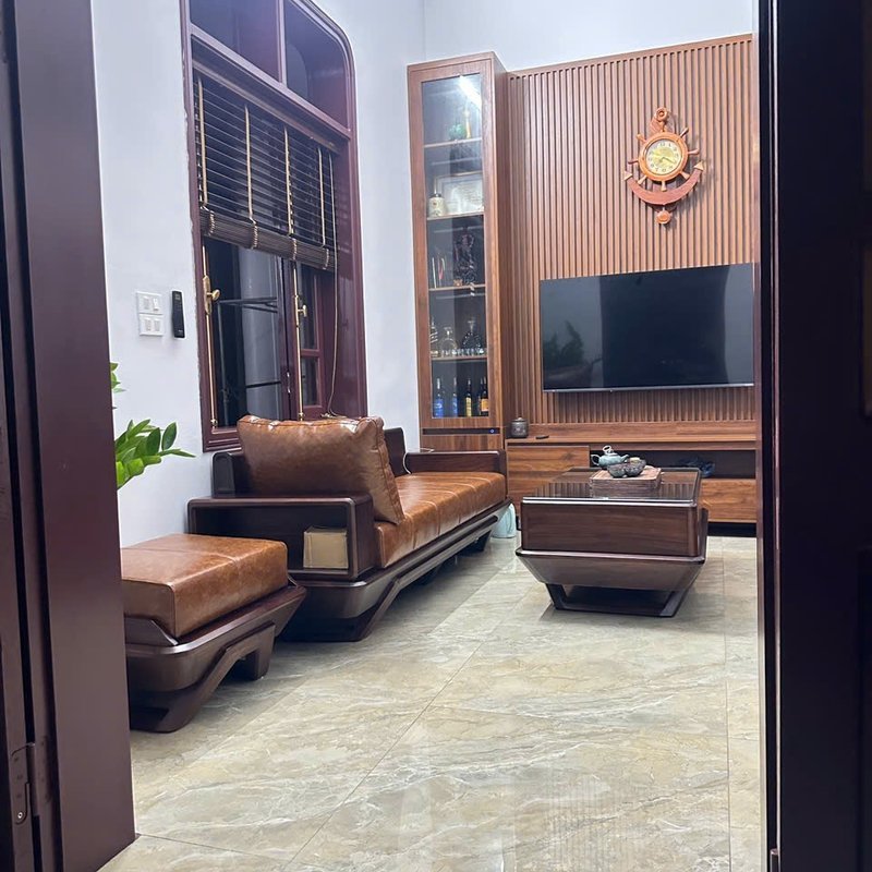 Phòng khách sau hoàn thiện nội thất: sofa da nâu, kệ tivi, vách lam gỗ và sàn đá bóng — công trình cải tạo của Nhà Mộc